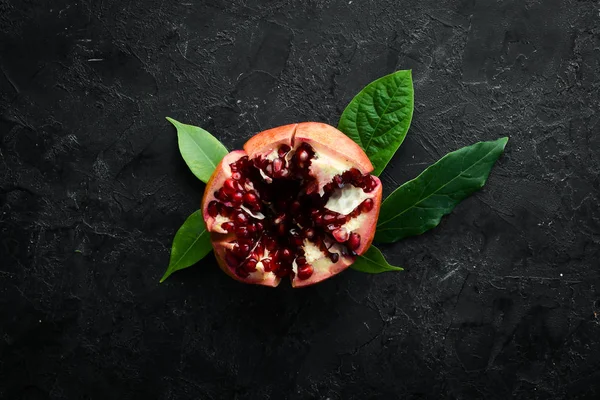 Siyah taş arka planda yaprakları olan taze nar. Meyveler. Üst Manzara. Metnin için boş yer.
