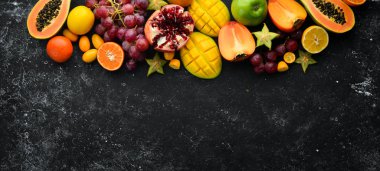 Fruits. Seasonal and tropical fruits on a black stone background. Food background. Top view. Free space for your text.