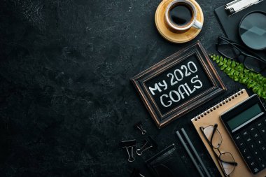 My goals 2020 text with office tools on a black desk. Top view. Free space for your text.