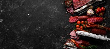 Salami and snacks. Sausage Fouet, sausages, salami, paperoni, on a black stone background. Top view. Free space for your text.
