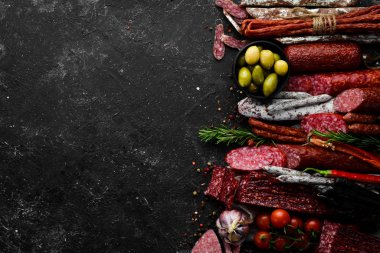 Salami and snacks. Sausage Fouet, sausages, salami, paperoni, on a black stone background. Top view. Free space for your text.
