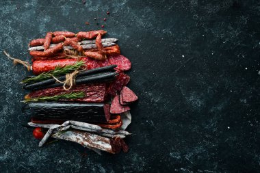 Salami and snacks. Sausage Fouet, sausages, salami, paperoni, on a black stone background. Top view. Free space for your text.