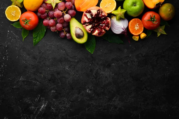 Vegetables and fruits, healthy food. Fruits and vegetables on black stone background. Tropical fruits. Top view. Free space for your text.