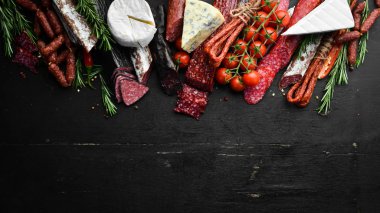 Assortment of cheese, salami, sausage, spices and meat products, on black background. Top view. Free space for your text.