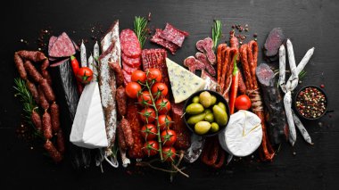 Assortment of cheese, salami, sausage, spices and meat products, on black background. Top view. Free space for your text.