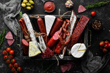 Assortment of cheese, salami, sausage, spices and meat products, on black background. Top view. Free space for your text.