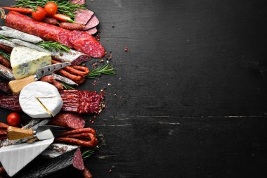 Assortment of cheese, salami, sausage, spices and meat products, on black background. Top view. Free space for your text.