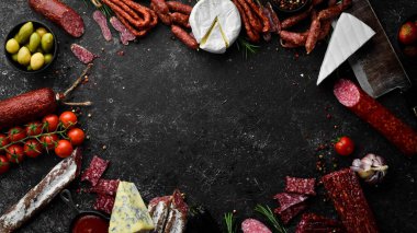 Assortment of cheese, salami, sausage, spices and meat products, on black background. Top view. Free space for your text.