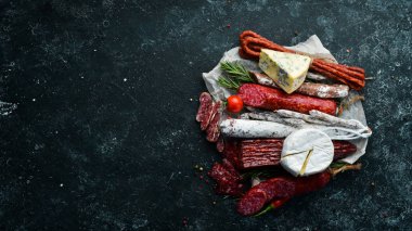 Assortment of cheese, salami, sausage, spices and meat products, on black background. Top view. Free space for your text.