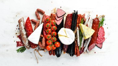 Assortment of cheese, dried salami and smoked sausages on a white wooden background. Top view. Free space for your text.