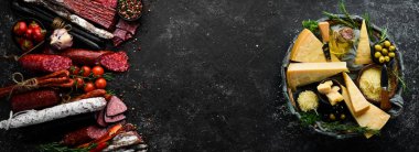 Background of salami, smoked sausage and assortment of cheese. On a black stone background. Free space for your text.