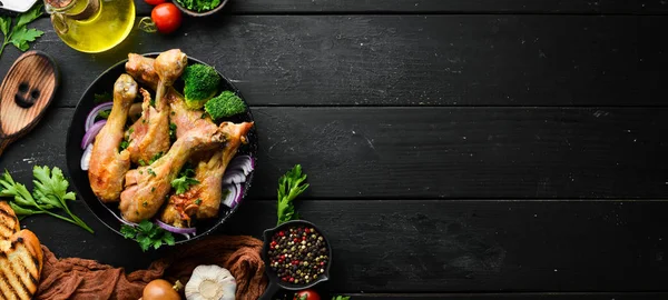 Baked chicken drumsticks with vegetables on a black plate. Chicken meat. Top view. Free space for your text.