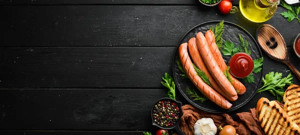 stock image Boiled sausage with ketchup on a black plate. Top view. Free space for your text.