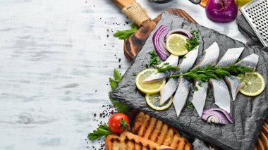 Siyah taş bir tahtanın üzerinde soğan ve limonla tuzlanmış ringa balığı. Üst Manzara. Metnin için boş yer.