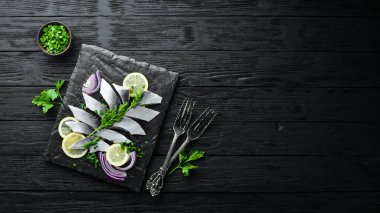 Siyah taş bir tahtanın üzerinde soğan ve limonla tuzlanmış ringa balığı. Üst Manzara. Metnin için boş yer.