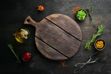 Kitchen board and vegetables with spices on black stone background. Top view. Free space for your text.