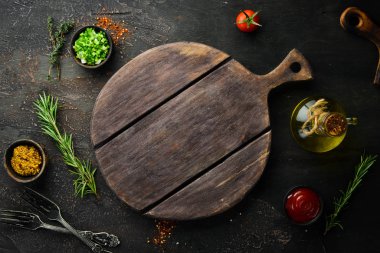Kitchen board and vegetables with spices on black stone background. Top view. Free space for your text.