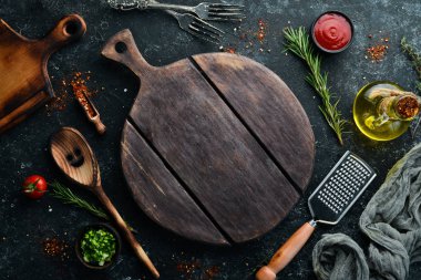 Kitchen board and vegetables with spices on black stone background. Top view. Free space for your text.