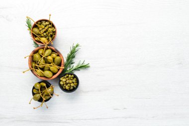 Beyaz ahşap arka planda bir kasede marine edilmiş kapari. Üst Manzara. Metnin için boş yer.