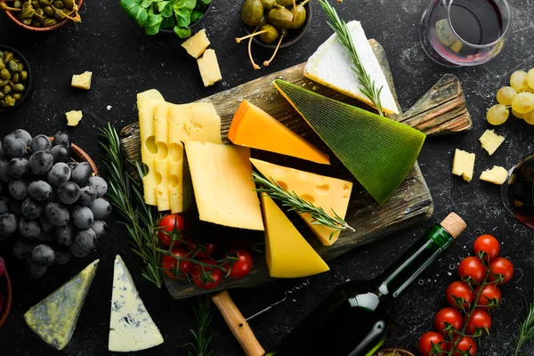 Wine, cheese and snacks on a black stone background. Assorted cheese. Top view. Free space for your text.