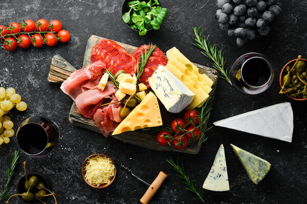 Italian appetizers. Cheese, wine, salami and prosciutto on a black stone background. Top view. Free space for your text.