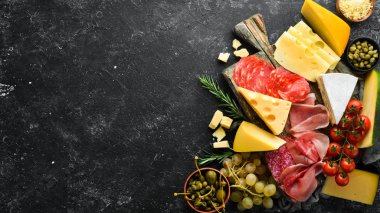 İtalyan atıştırmalıkları ve bardakta şarap olan aperatifler. Peynir, şarap, salam ve siyah taştan bir arka planda jambon. Üst Manzara. Metnin için boş yer.