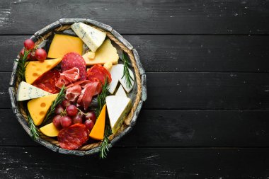 İtalyan atıştırmalıkları ve bardakta şarap olan aperatifler. Peynir, şarap, salam ve siyah taştan bir arka planda jambon. Üst Manzara. Metnin için boş yer.