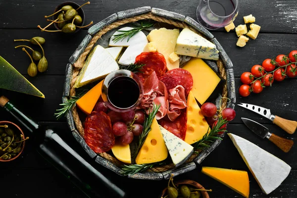 Appetizers table with italian antipasti snacks and wine in glasses. Cheese, wine, salami and prosciutto on a black stone background. Top view. Free space for your text.