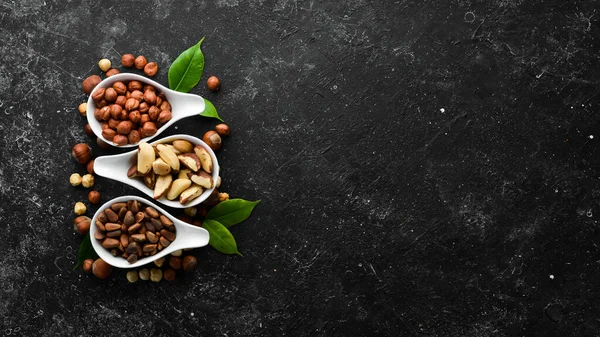 Assortment of nuts: pistachios, hazelnuts, pine nuts on a black stone background. free space for your text. Top view.