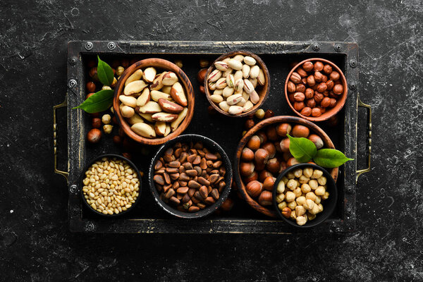 Assortment of nuts: pistachios, hazelnuts, pine nuts on a black stone background. free space for your text. Top view.