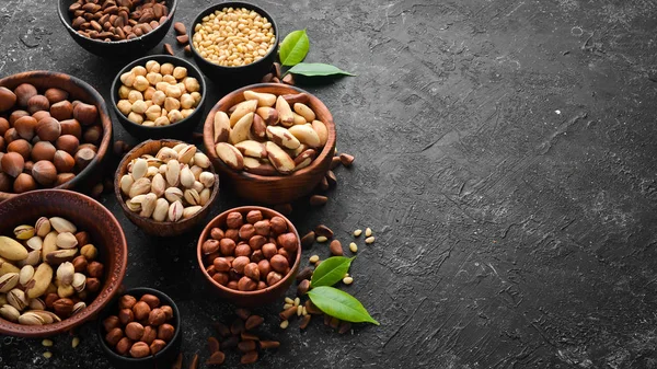 Assortment of nuts: pistachios, hazelnuts, pine nuts on a black stone background. free space for your text. Top view.