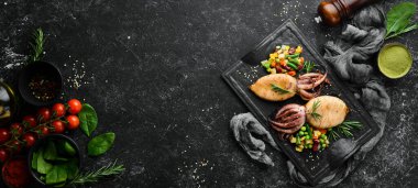 Siyah taş bir tabakta sebzeli pişmiş mürekkep balığı. Deniz ürünleri. Üst Manzara. Metnin için boş yer.