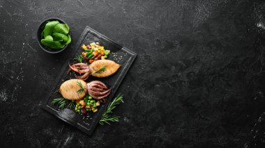 Siyah taş bir tabakta sebzeli pişmiş mürekkep balığı. Deniz ürünleri. Üst Manzara. Metnin için boş yer.