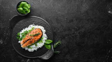 Siyah taş tabakta pilav ve sebzeli somon bifteği. Deniz ürünleri. Üst Manzara. Metnin için boş yer.