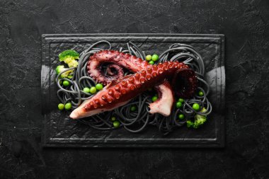 Siyah taş tabakta ahtapot dokunaçlı siyah makarna. Deniz ürünleri. Üst Manzara. Metnin için boş yer.