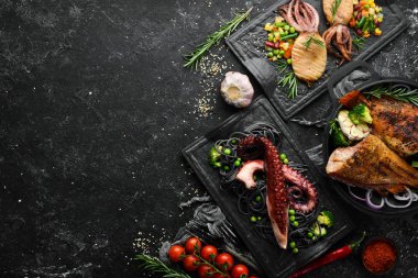 Deniz ürünleri tabakları. Siyah taş zemin üzerinde balık, mürekkep balığı, ahtapot. Üst Manzara. Metnin için boş yer.