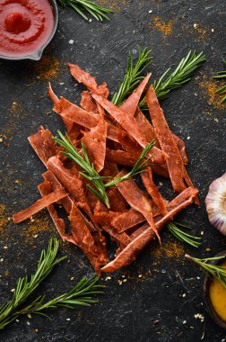 Kurutulmuş. Baharatlı ve otlu kurutulmuş et dilimleri. Siyah bir arka planda bira için atıştırmalıklar. Üst görünüm.