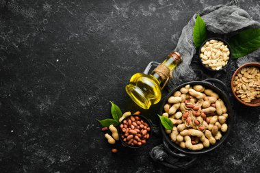 Fıstık yağı soğuk basınçlıdır. Siyah taşlı arka planda yer fıstıkları. Üst görünüm