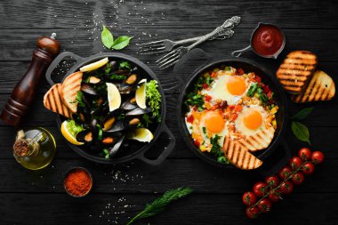 Siyah arka planda kızartma tavasında tabak seti. Kızarmış yumurta ve midye. Üst görünüm.