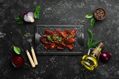 İtalyan yemeği. Siyah bir tabakta taze bitki ve baharatla kurutulmuş domatesler. Üst görünüm.