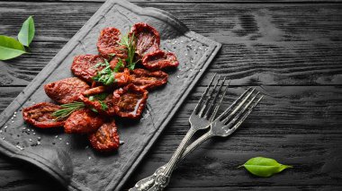 İtalyan yemeği. Siyah bir tabakta taze bitki ve baharatla kurutulmuş domatesler. Üst görünüm.