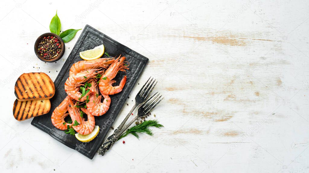 Boiled shrimp with parsley and lemon on a black stone plate. Top view. Seafood.