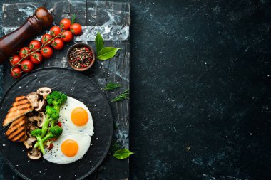 Sağlıklı kahvaltı. Brokolili yumurta, mantar ve ekmek. Siyah taştan bir tabakta. Üst görünüm.