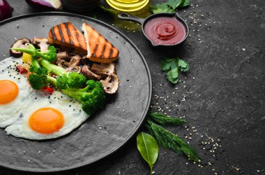 Sağlıklı kahvaltı. Brokolili yumurta, mantar ve ekmek. Siyah taştan bir tabakta. Üst görünüm.