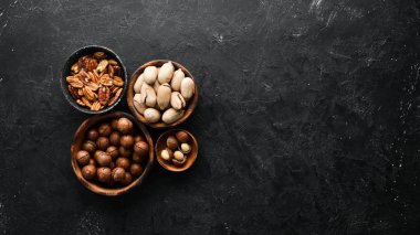 Siyah taş arka planda kaselerde egzotik cevizler ve macadamia fındıkları. Üst Manzara. Metnin için boş yer.