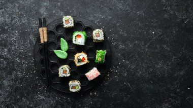Siyah taşlı arka planda deniz mahsulleri olan büyük bir suşi sarması. Üst Manzara. Metnin için boş yer.