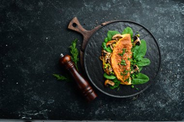 Mantarlı omlet ve siyah tabakta ıspanak. Üst Manzara. Metnin için boş yer.