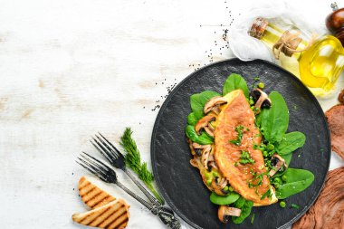 Mantarlı omlet ve siyah tabakta ıspanak. Üst Manzara. Metnin için boş yer.