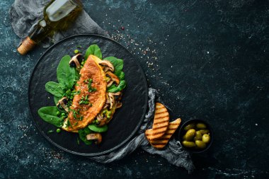 Mantarlı omlet ve siyah tabakta ıspanak. Üst Manzara. Metnin için boş yer.