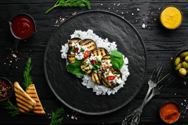 Siyah tabakta pilav ve peynirle kızartılmış patlıcan. Üst Manzara. Kırsal biçim.
